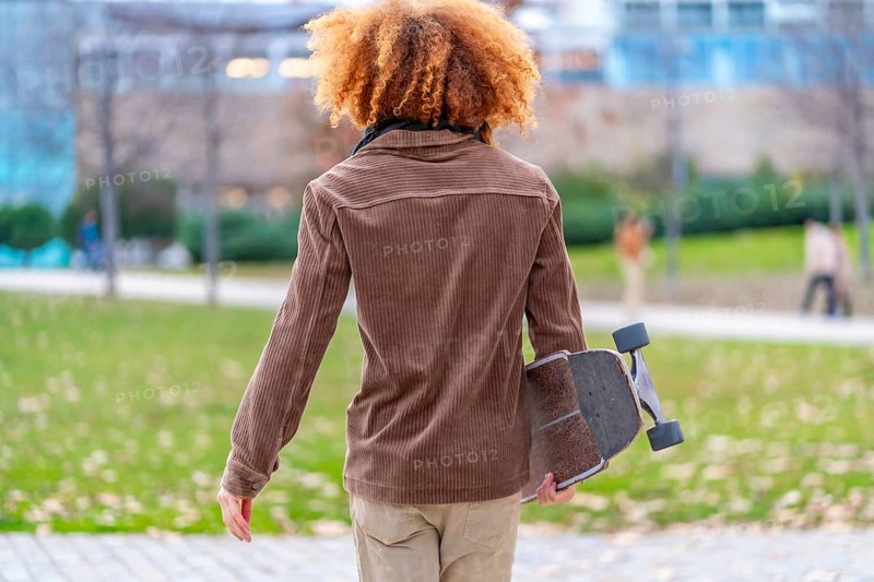 Rear view of a man carrying a skateboard in a park