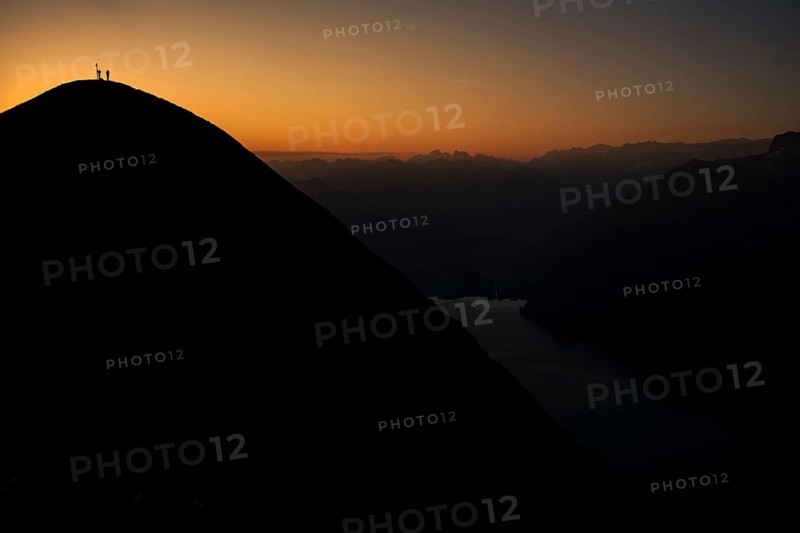 Mountaineer on ridge with Swiss mountains and Lake Thun in the background at sunrise