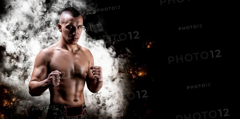 Portrait of a boxer of mixed martial arts standing on the background of smoke and fire. The concept of sports