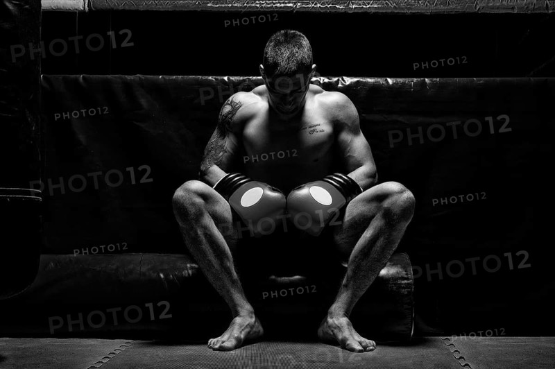 Boxer sits in gloves near the ring with his head bowed. The concept of sports