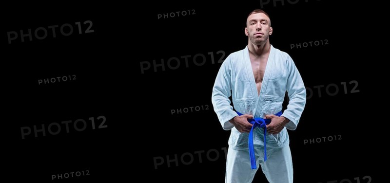 Professional athlete stands in the gym in a kimono with a blue belt. Concept of karate