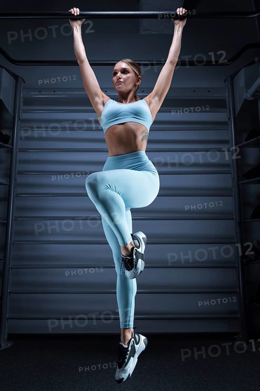 Athletic girl pulls up on the bar in the gym on a blue background. The concept of sports
