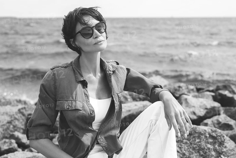 Portrait of a stylish woman sitting on stones in the bay. Windy weather. Happiness