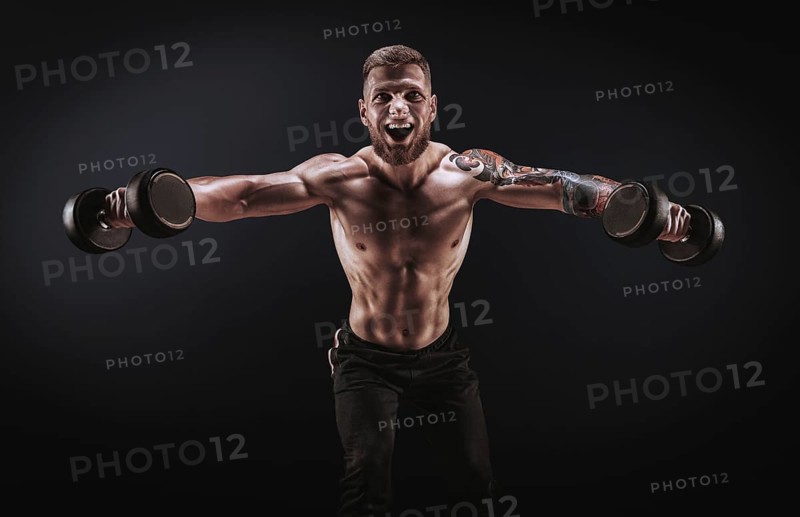 Handsome young man spreads his arms with dumbbells to the sides. Shoulder pumping. Fitness and bodybuilding concept.