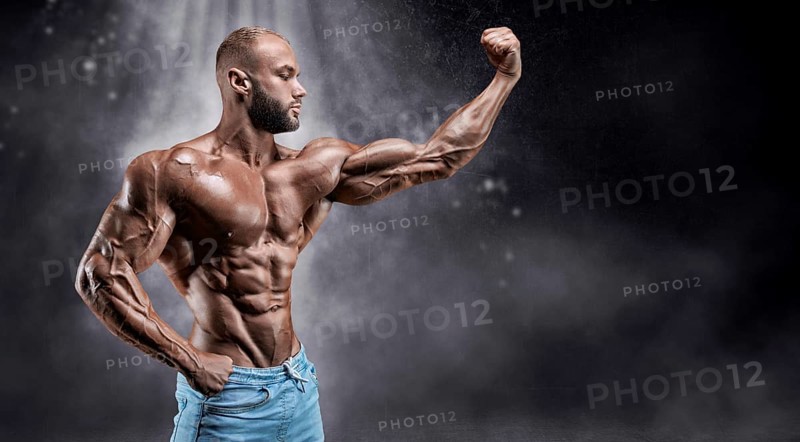 Isolated athlete on a background of smoke with small dust particles. Bodybuilding concept.