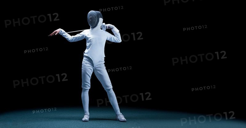 Charming girl dressed as a fencer posing with a mask and a sword. The concept of fencing.