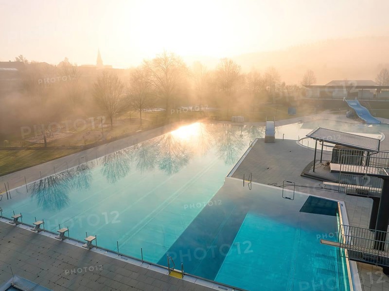 Morning light reflected in the water of a fog-covered swimming pool with slides
