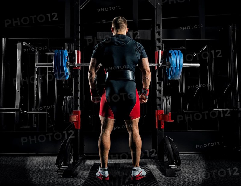 Professional athlete stands in front of the bars with a barbell and is about to crouch with her. Back view