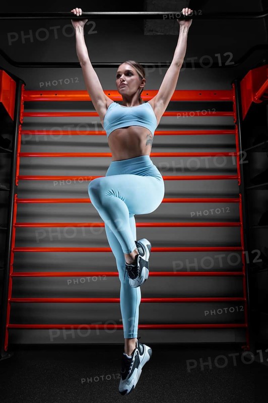 Beautiful tall blonde pulls up on the bar in the gym against the backdrop of the wall bars. The concept of sports