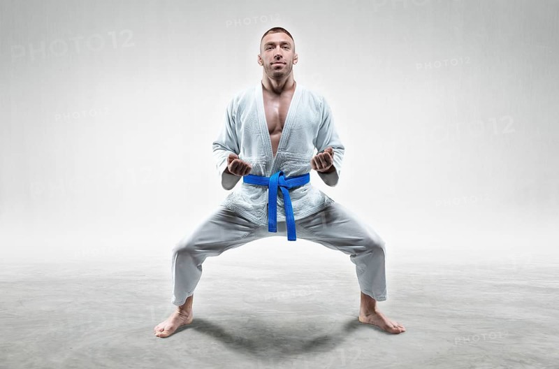 Athlete in a kimono with a blue belt stands in a fighting position. Concept of karate