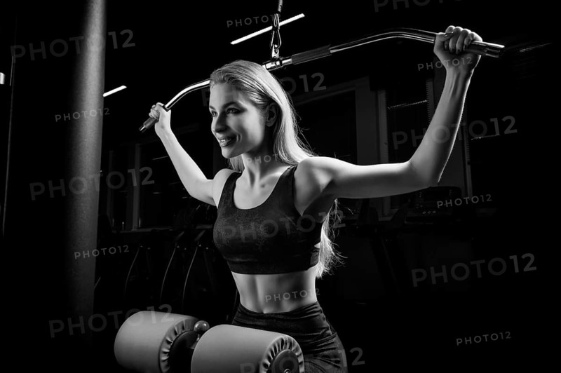 Charming blonde does exercises for the back in the gym. Neck pull for the head. The concept of sports