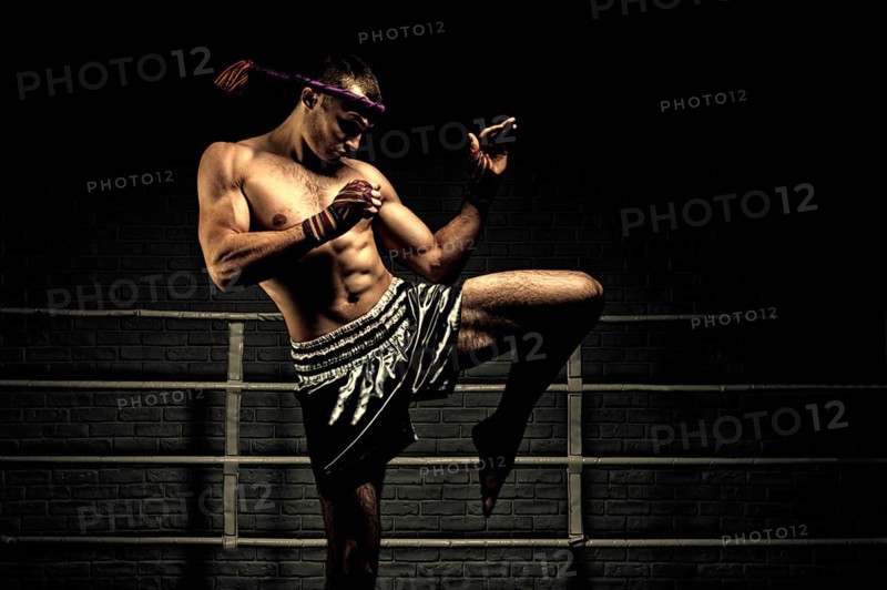 Kickboxer in the ring surrounded by searchlights stretches before the fight. Makes swing movements with his knee. Mongkhon.
