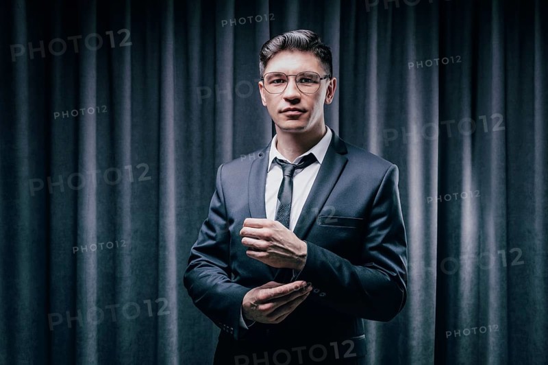 Adult man is standing in a suit against a black curtain. Business concept. The administrative staff of the company.