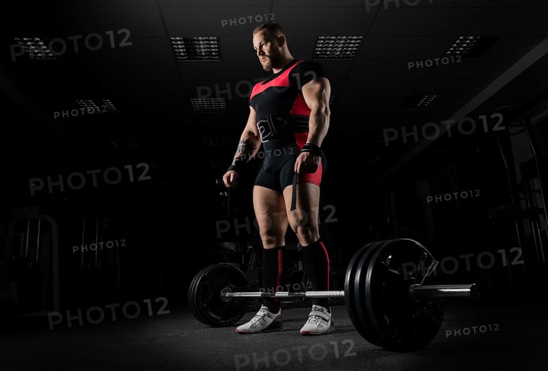 The weightlifter is preparing to perform an exercise called deadlift. He stands directly above the barbell and looks at it