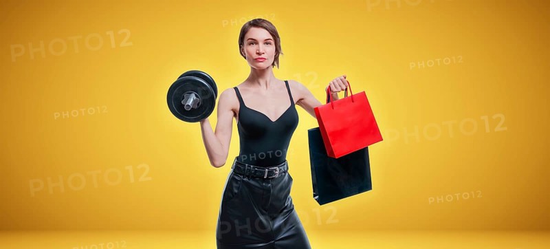 Beautiful slender woman posing in the studio with a dumbbell and gift bags. Gift concept. Gym membership