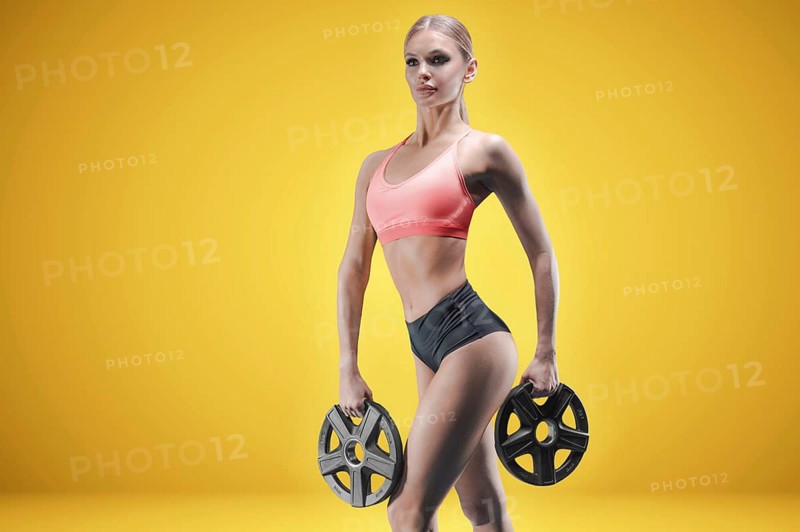 Portrait of a tall athletic woman with weight plates in her hands. The concept of sports