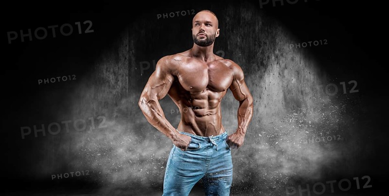 Isolated athlete on a background of smoke with small dust particles. Bodybuilding concept.