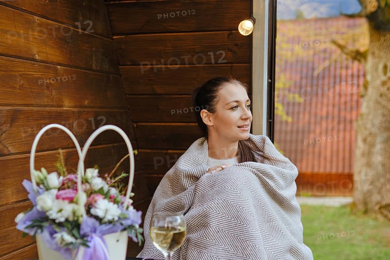 Woman wrapped in plaid sitting on veranda looks away with interest