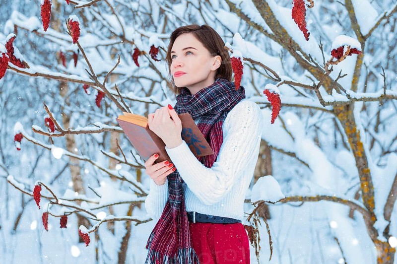 Portrait of a charming girl who reads a book in the winter forest. Concept of Christmas