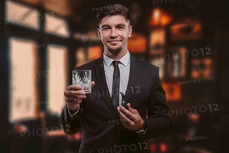 Portrait of an elegant man in a suit with a smoking pipe and a glass in a restaurant. Business concept.