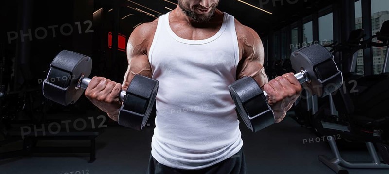Portrait of a man in a white T-shirt exercising in the gym with dumbbells. Biceps pumping. Fitness and bodybuilding concept.