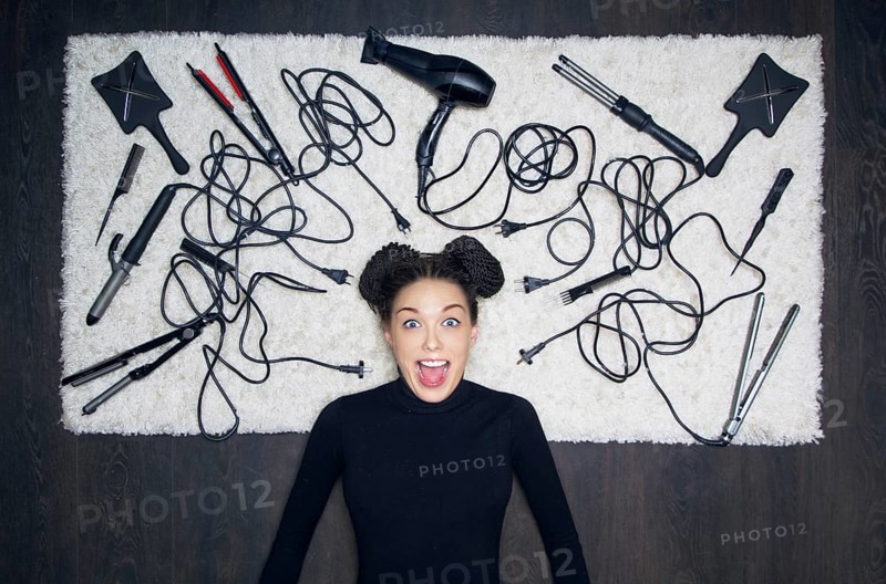 Young charming girl with dreadlocks on her head is shouting in surprise. The girl is lying on a white carpet. Around the tools for creating a haircut