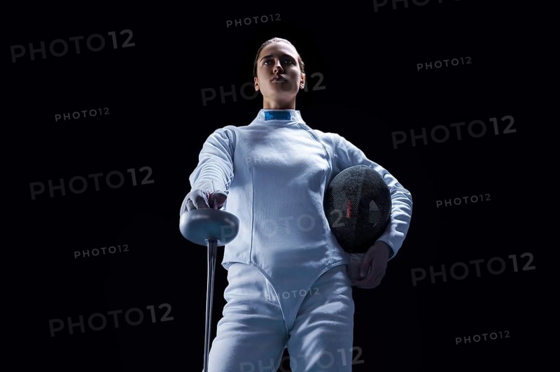 Charming girl dressed as a fencer posing with a mask and a sword. The concept of fencing.