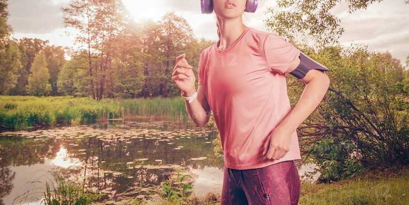 Portrait of a beautiful girl running in a sunny park in headphones with a smartphone. Music apps concept.
