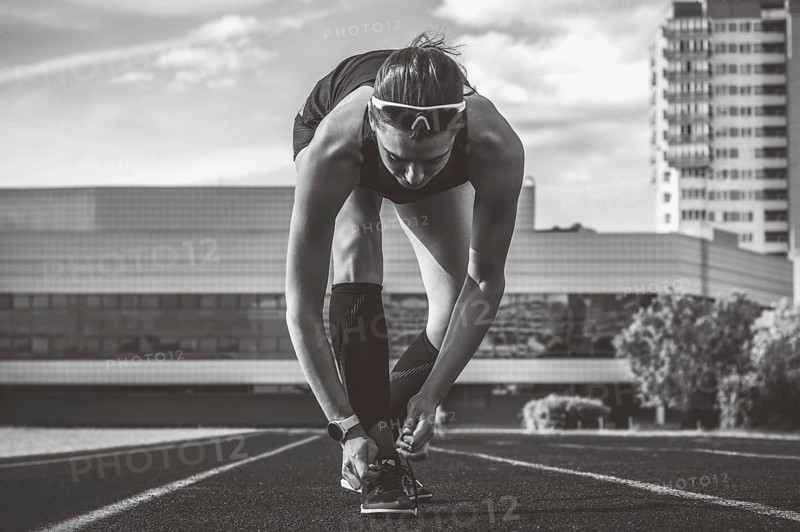 Image of a young female runner laces her shoes on a stadium track. Sports concept.