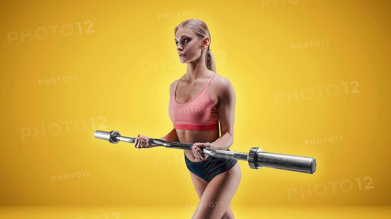 Charming tall athlete posing in the studio on a yellow background with a barbell in her hands. The concept of sports