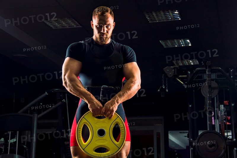 Huge weightlifter stands with a weight in his hands in the gym