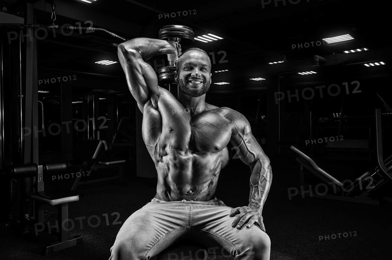 The athlete is doing the exercise in the gym. Lifting a dumbbell with one hand from behind the head. Fitness