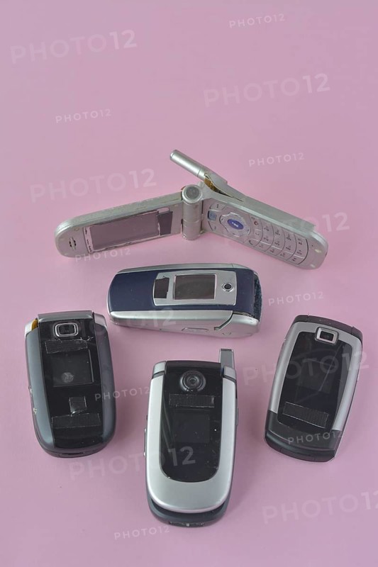 A birds-eye view of classic flip phones on a plain pink background