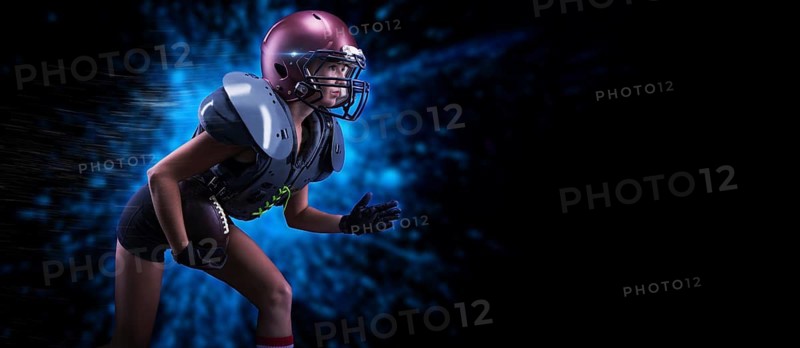 Image of a girl in the uniform of an American football team player. She runs with the ball against the background of light spots. Sports concept. Shoulders pads.