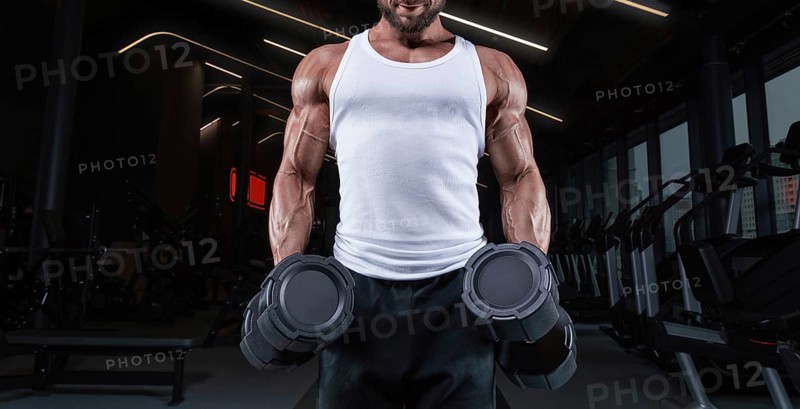 Handsome young man working out with dumbbells in the gym. Shoulder pumping. Fitness and bodybuilding concept.