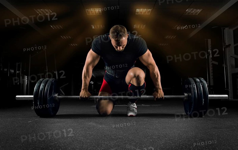 Athlete is standing on his knee and near the bar in the gym and is preparing to make a deadlift