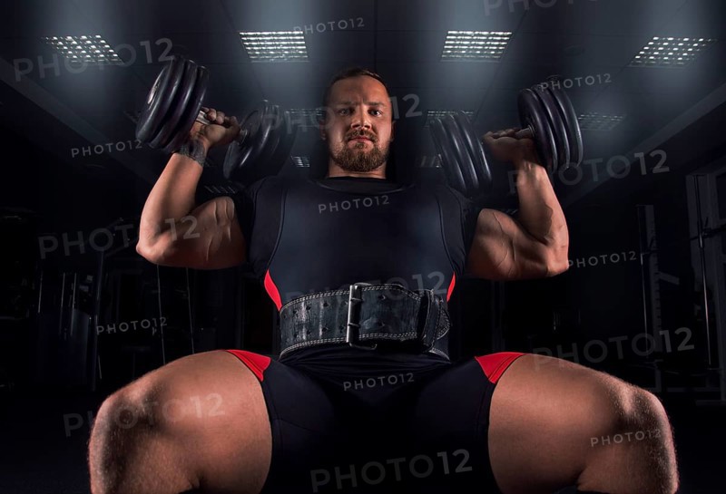 The athlete sits on a bench in the gym and does an exercise called military press