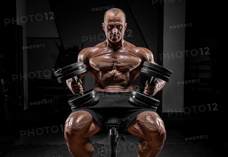 Muscular man sits on a bench with dumbbells. Bodybuilding and powerlifting concept.