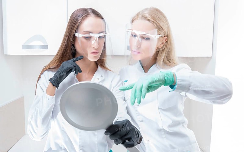 Two beauticians pose in a medical salon with a mirror in their hands. Rejuvenation concept.