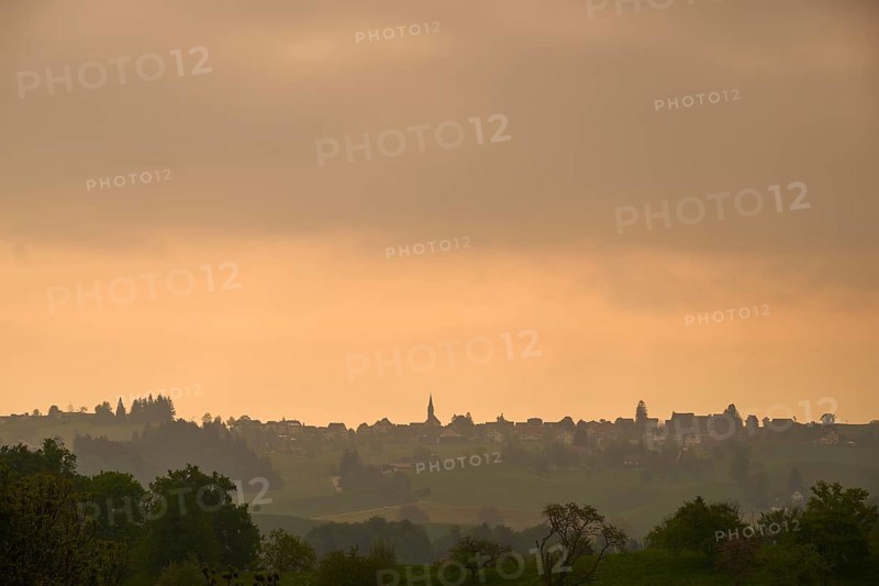 Silhouette of a village on a hill under an orange-coloured sky at sunrise