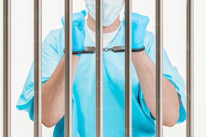 Doctor in handcuffs is standing behind a prison cell. The concept of corruption in medicine.