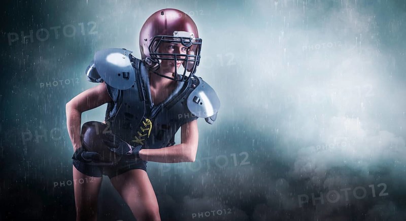 Image of a girl in the uniform of an American football team player. She runs with the ball against the background of light spots. Sports concept. Shoulders pads.