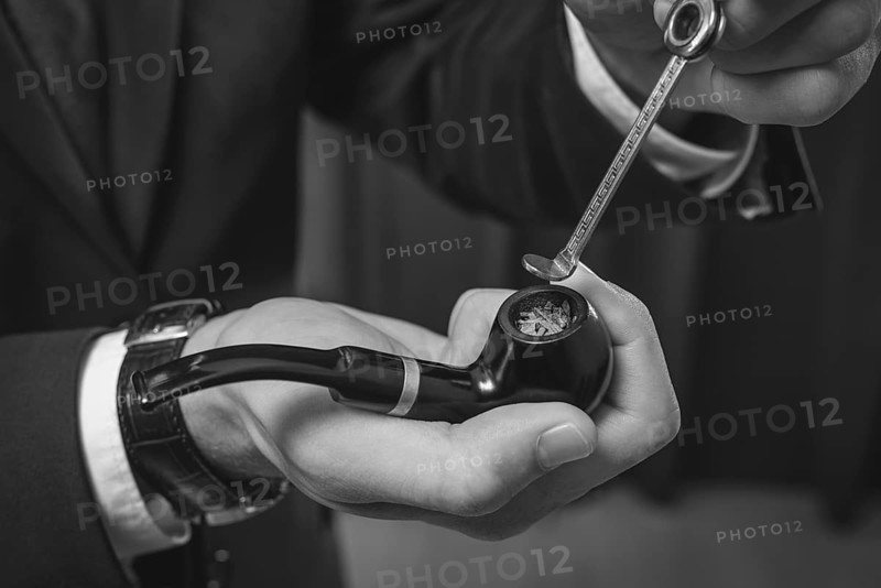 Image of male hands holding a smoking pipe and tamper. Tobacco smoking concept.