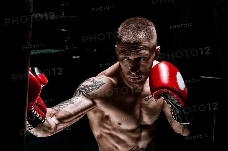 Professional boxer hits the bag against the background of the ring. Side view. The concept of sport and classic boxing.
