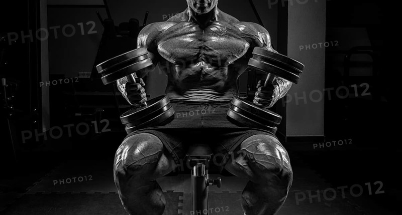 Muscular man sits on a bench with dumbbells. Bodybuilding and powerlifting concept.