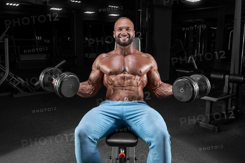 The athlete is doing the exercise in the gym. Lifting dumbbells while sitting on a bench. Fitness