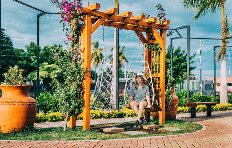 Beautiful girl in hat sitting on a white swing in a beautiful garden. Portrait of a smiling girl sitting on a swing in La Calzada