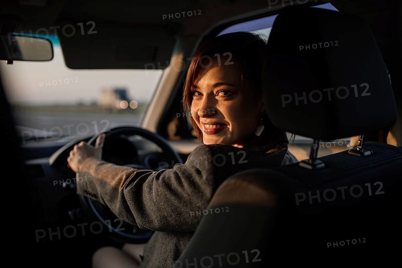 Young beautiful smiling female taxi driver in a jacket greets passengers in a friendly manner