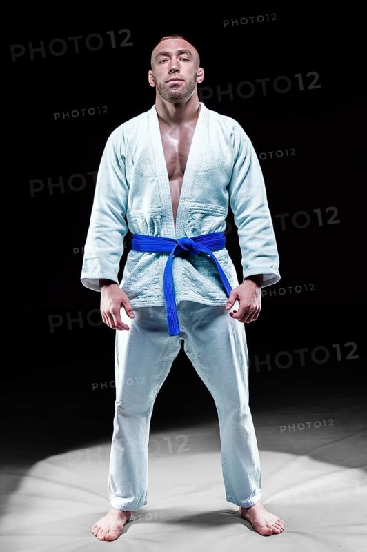 Professional athlete stands in the gym in a kimono with a blue belt. Concept of karate