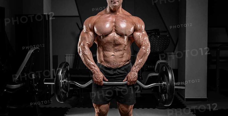 Powerful bodybuilder trains in a gym with a barbell. No name portrait. Bodybuilding concept.
